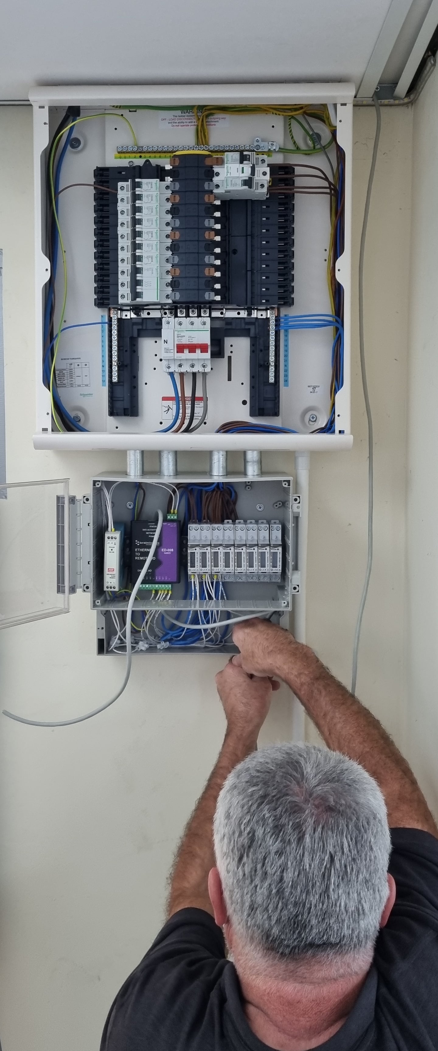 Electrician installing energy monitoring enclosure with BB-400 and sub meters below a power distribution panel